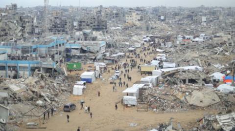 Aerial view of Gaza, with buildings and rubble as people walk down road