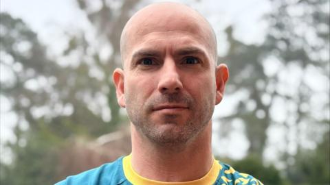 Chris Fordham, wearing a green and yellow T-shirt, stood in front of trees on a grey day.