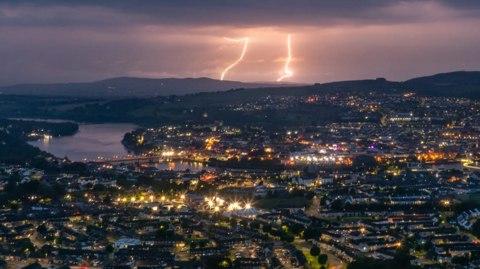 Shows bolts of lightning above a city at nighttime