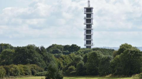 A large grey communications tower rises out of an area of woodland in Purdown.