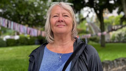 Loren Wilson wearing a black coat with blue top and necklace. She has blonde hair.