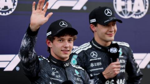 Kimi Antonelli waves to fans with Mercedes team-mate George Russell in the background after Japanese Grand Prix qualifying