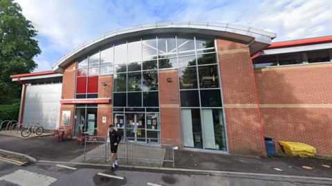 The entrance of a leisure centre. It has a curved roof and lots of windows.