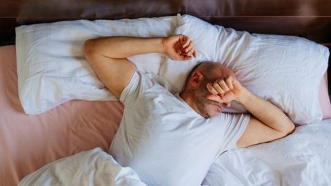 Man waking up in bed covering eyes feeling tired - stock photo
