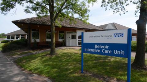 The exterior of the Belvoir Intensive Care Unit which is a single storey brick building with a blue NHS sign outside the front.