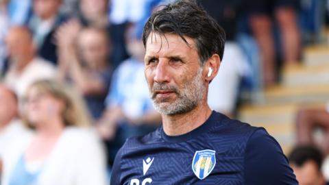 Danny Cowley pitchside. He had short dark hair and is wearing a navy blue Colchester United training shirt.