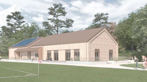 An artist's impression shows a new building with a pitched roof and large windows. There is huge solar panel on the left hand side of the roof.
The building is beside a sports pitch with a flag on the corner of a marked sports area. There are images of people running on a path beside the building, standing nearby or sitting on a bench looking towards the pitch.