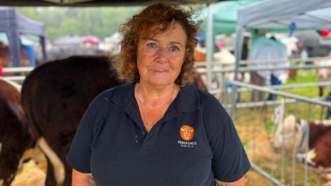 A woman with redish brown hair looking at the camera, she has a navy polo top