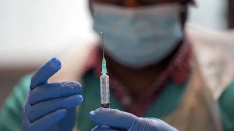 A medic in scrubs holding a needle