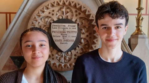 Chanel (left), who is wearing a brown cardigan and white T-shirt stands beside Thomas is wearing a blue jumper