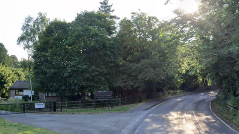 A road through a wooded area with a sign on the left saying Roslin Glen