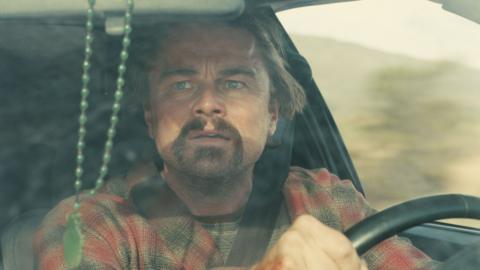 Leonardo DiCaprio is seen in an image from his film at the steering wheel of a car, with a goatee and wearing a plaid shirt.
