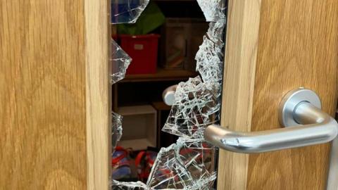 A close up of a door with a glass centre which has been smashed. Chips on the chrome door handle can be seen.