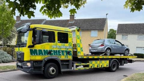 A silver car on the back of a recovery truck.
