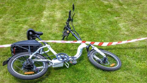 An e-bike lying on grass with a red and white tape over the top