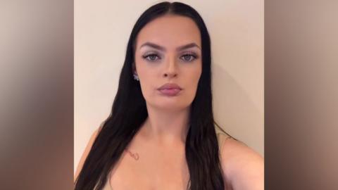 Portrait shot of woman with dark hair against a wall.