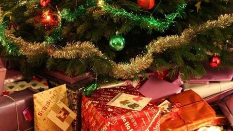 A close-up of wrapped presents beneath a tree with tinsel and decorations.