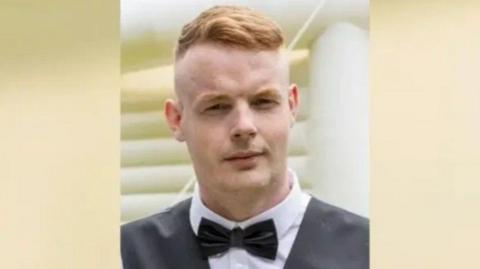 A head and shoulders shot of Lewis Bell wearing a black bowtie and waistcoat. He has short ginger hair.