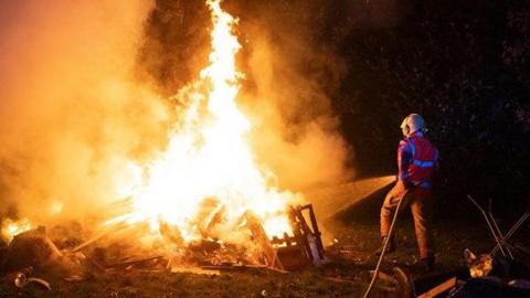 A fireman puts out a bonfire at night. 