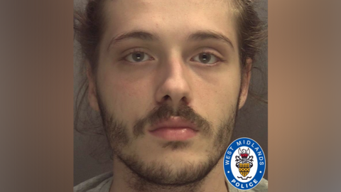 A police mugshot of a man with a beard and brown hair. He is looking directly at the camera. There is a West Midlands Police emblem in the bottom right hand corner of the image.