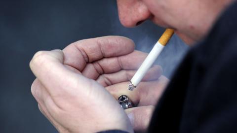 A man cupping a lighter in his hands as he attempts to light a cigarette.