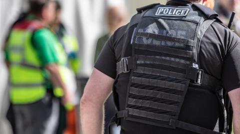 A polic officer wearing a vest over their back. Paramedics can be seen in the background.