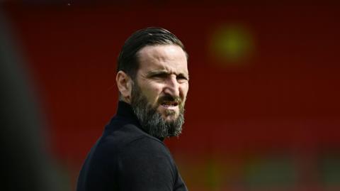 Notts County head coach Martin Paterson wearing a black jumper. He has a beard and slicked back hair