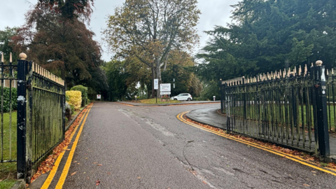 The entrance to Cannon Hill Park in Moseley. Two gates open onto a road leading into a tree-lined area.