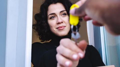 A woman in a black jumper is handed a key with a yellow tag while standing in a doorway
