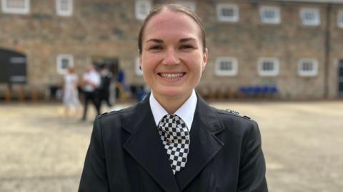 Woman in States of Jersey Police uniform smiling in front of a brick building