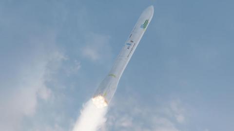 A white rocket flying through the air. Blue sky in the background. There is fire and fuel coming out of the rocket itself.
