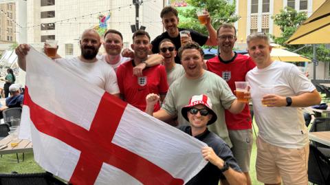 England fans are drinking beer in a square in Dallas in front of a St George's Cross