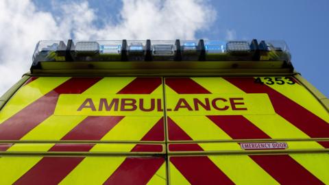 The rear of an ambulance with red and fluorescent yellow chevrons and blue lights on the roof.