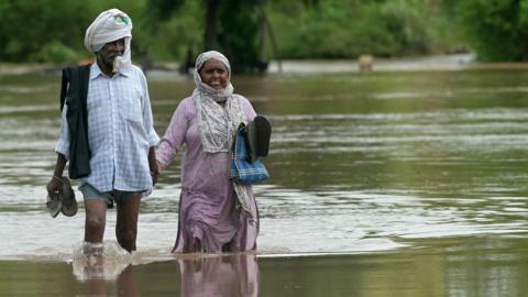 A man and a woman wade through floodwaters after the Ravi river overflowed following heavy rains in a village near Ajnala in Punjab, on August 30, 2025