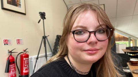 A young woman with blond hair, wearing glasses.