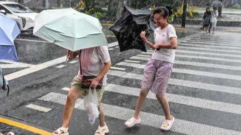 People use umbrellas to shelter from the rain as they walk on The Bund a day after Typhoon Dolphin made landfall in Shanghai on August 10, 2026.