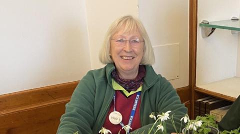 A woman sat in front of a plant on a table.