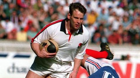 Ian Hunter in an white England shirt carrying a rugby ball in a match