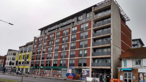 Red brick block of apartments in High Street, Slough, with seven floors about a row of shops.