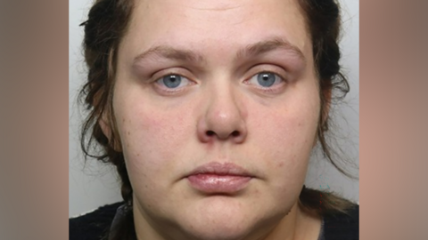 A mugshot of a woman with brown hair and wearing a dark top.