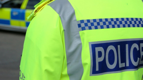 An unidentifiable police officer is pictured from behind with a police car in front of him