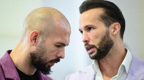 Andrew Tate stands next to his brother Tristan Tate - each wearing pastel suit jackets and white shirts - inside Bucharest's court of appeal