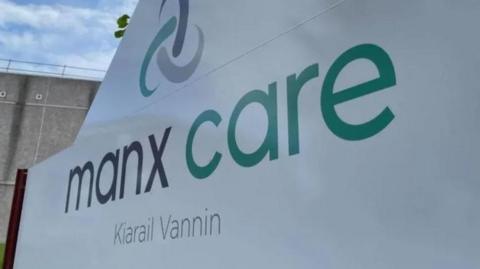 A close-up of a white sign that reads Manx Care in grey and green lettering, with the Manx translation underneath.