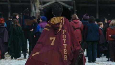 Harry facing away form the camera wearing a read quidditch cloak with golden letters saying 7 and Potter 