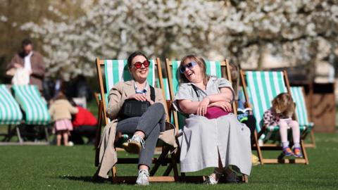 People sitting in deck chairs in a park enjoying some spring sunshine.