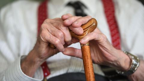 A close up of the hands of an elderley gentleman who is holding onto a walking stick. 