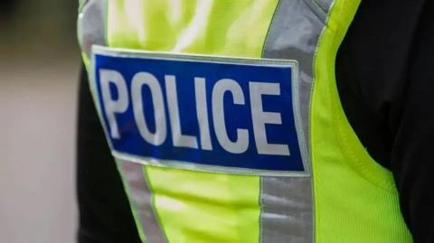 The back of a police officer who is wearing a high-vis neon vest over a black jacket