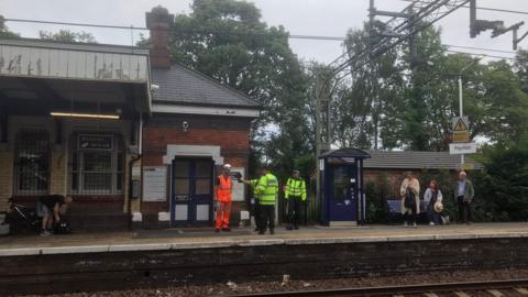 Police and railway engineers talk to commuters on the platform at Poynton railway station