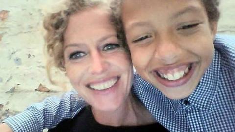 A picture of Fiona Donohoe with her son, Noah. Both are smiling at the camera. Fiona has curly, blonde hair which is tied back and Noah is wearing a blue and white checkered shirt.