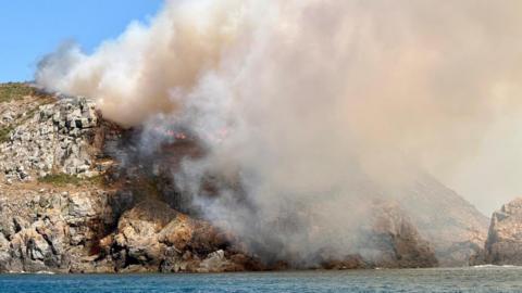A close ip picture of Little Sark - there is a large white plume of smoke. There are small amounts of orange flame.